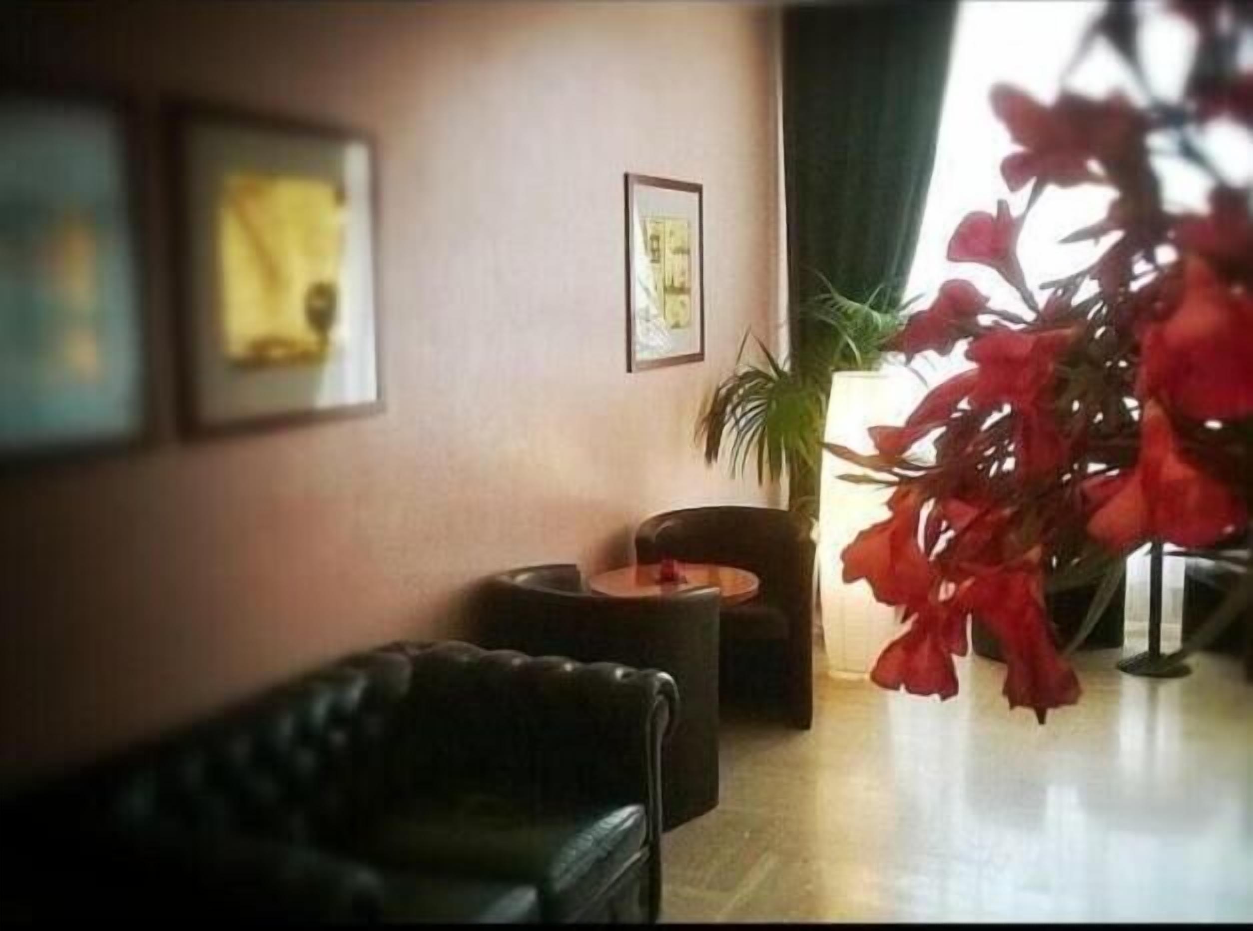 Una habitación con un sofá de cuero negro, una pequeña mesa redonda y una planta en maceta.