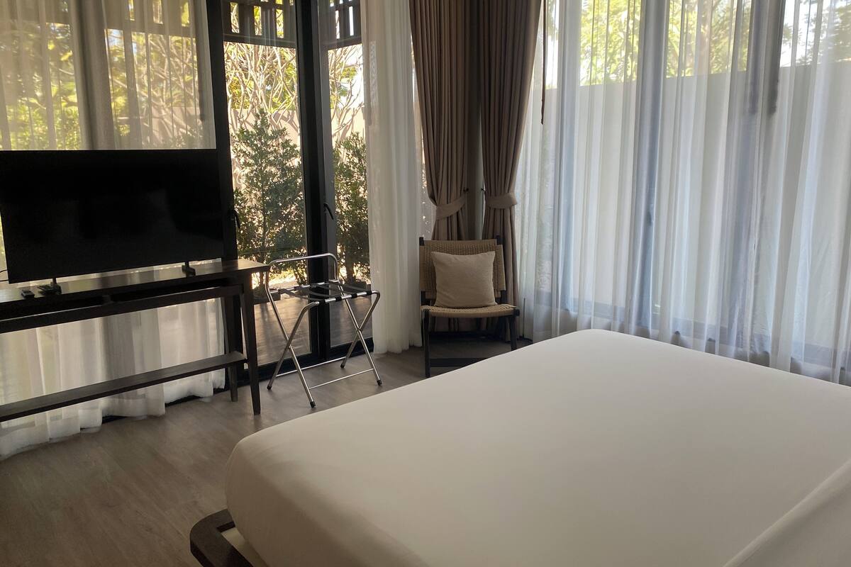 Habitación de hotel con cama, televisor sobre un mueble, una silla y ventana con cortinas.