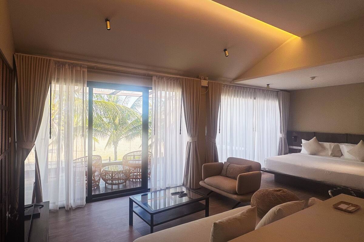 Una habitación de hotel con cama, sofá, mesa de centro y balcón con cortinas.