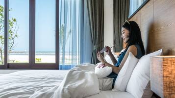 A person lying on a bed in a room with a large window, reading a book.