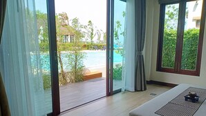 Habitación de hotel con ventana grande, cama y vista a una piscina y vegetación.