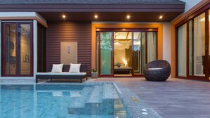 Un área de piscina exterior moderna con un sofá y una silla de mimbre, una puerta de cristal que da a un dormitorio y una entrada bien iluminada.
