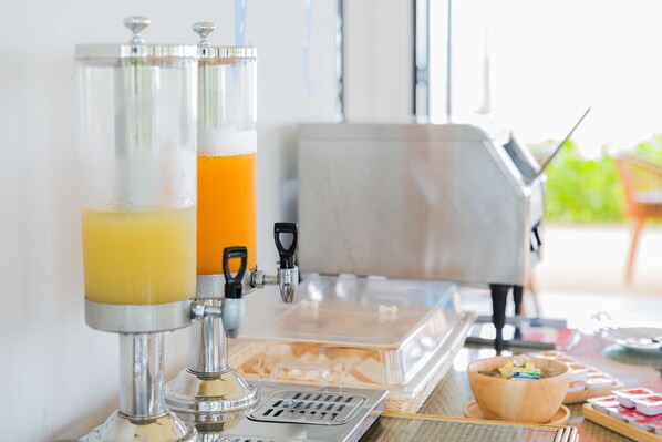 A beverage dispenser with two taps, a coffee machine, and a buffet area with food containers.