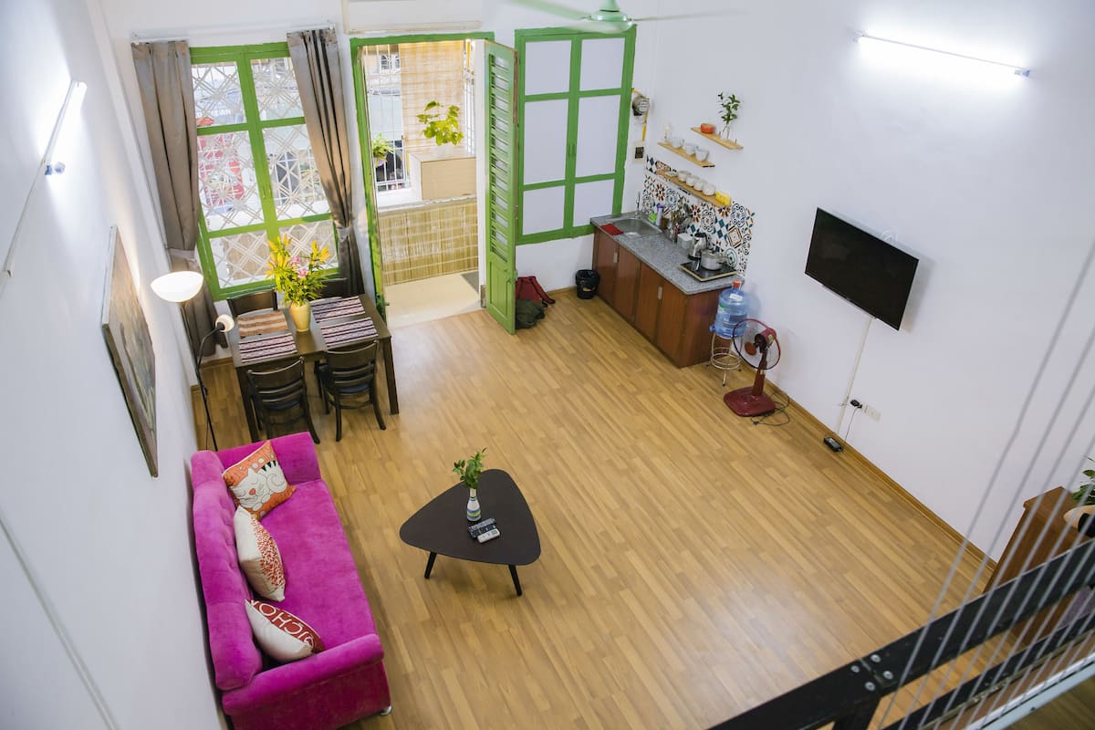 Un espace de vie compact avec un canapé rose, une petite table basse noire, un téléviseur fixé au mur et un plancher en bois.