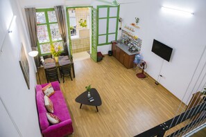 A compact living space with a sofa, a small coffee table, a TV mounted on the wall, and a kitchen area with a water dispenser.