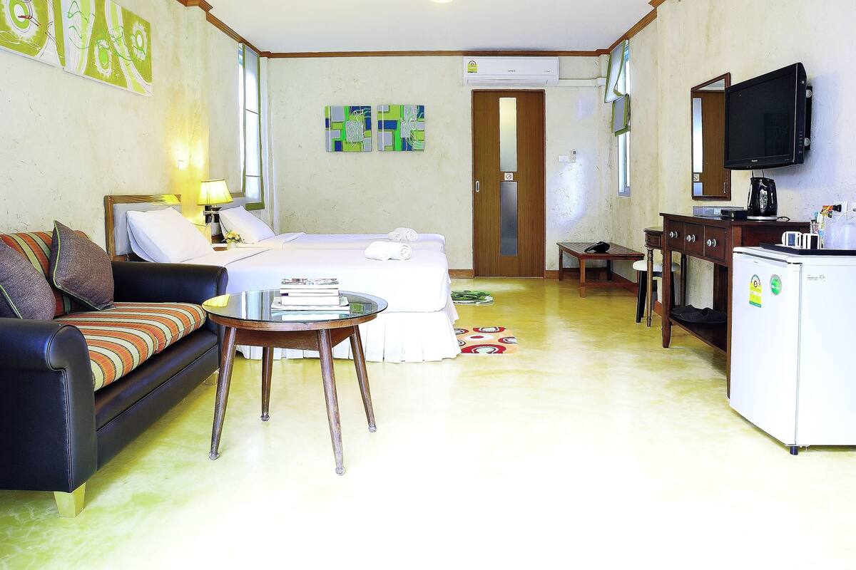 Une chambre d’hôtel comprenant un lit, un canapé, une petite table, un bureau avec un miroir, une télévision et un réfrigérateur.
