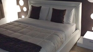 Un dormitorio moderno con una cama blanca, almohadas oscuras y una colcha estampada.