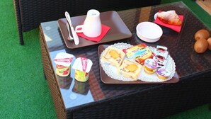 Un sofá de mimbre con cojines verdes, una mesa de vidrio con comida y bebidas, y una puerta de madera al fondo.