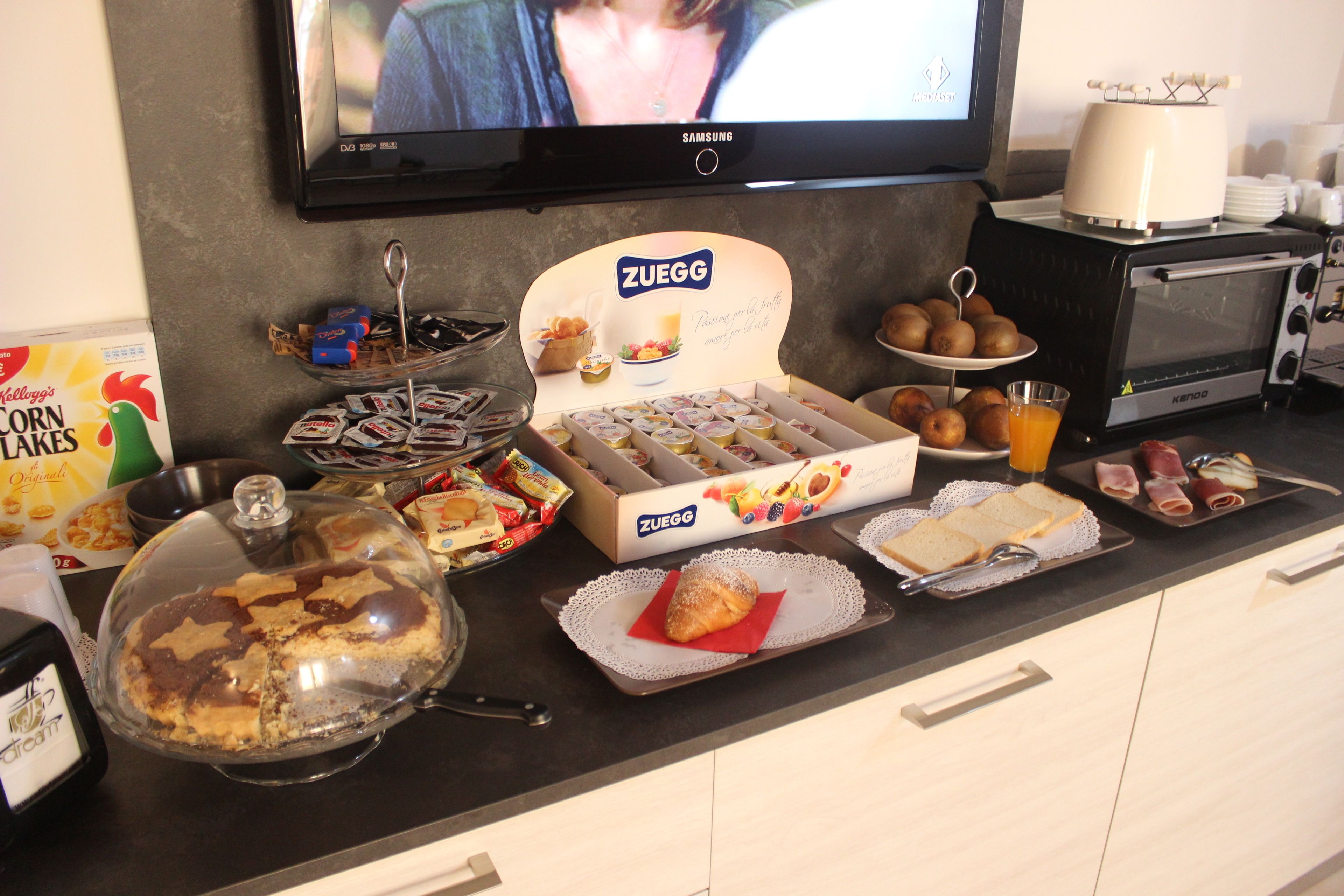 A breakfast buffet with various food items and a television displaying a scene.