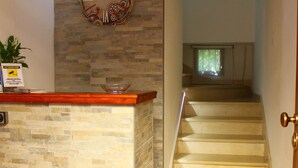 Zona de recepción con pared de piedra, un reloj y una escalera que sube a un nivel superior.