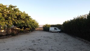 A white van parked in a gravel area with a hedge on one side and a building in the background. - Le Baronie (Scicli)