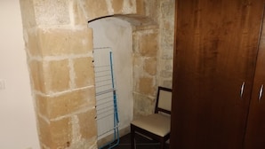 A room with a stone wall, a wooden door, a chair, and a blue rack. - Le Baronie (Scicli)