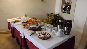 A buffet table with various food items, a cake, coffee pots, and a decorative plant. - Le Baronie (Scicli)