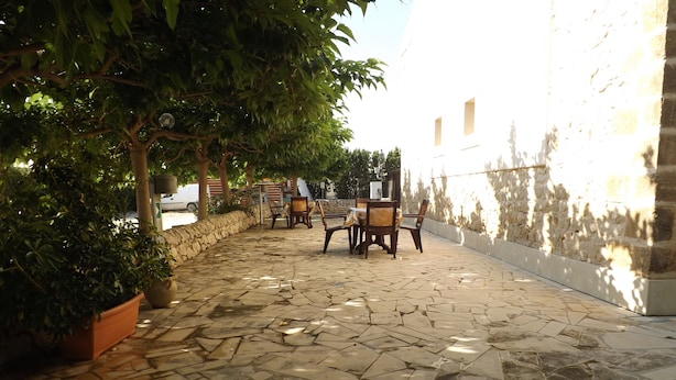 A stone-paved patio with outdoor furniture, surrounded by trees and a stone wall. - Le Baronie (Scicli)