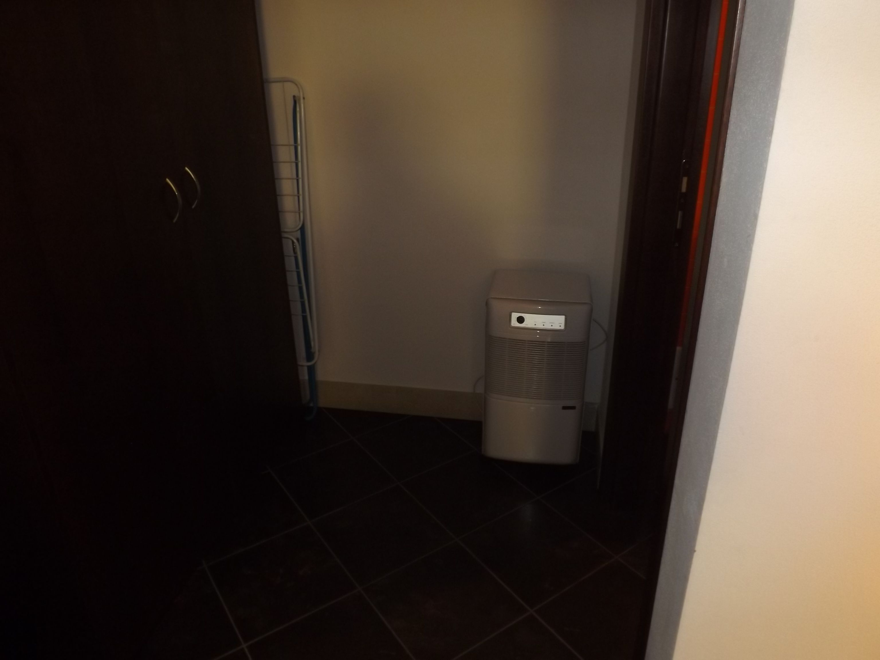 Un couloir étroit avec un radiateur blanc adossé à un mur, une porte sur la gauche et un sol carrelé.