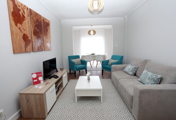 A modern living room with a flat-screen TV, two teal armchairs, a grey sofa, and a white coffee table. - Apartments 27 Mae de Deus by Green Vacations (Ponta Delgada)