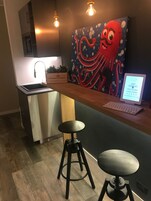 Eine moderne Küche mit einer Holzausziehtafel, einem Spülbecken und einem Bild von einem Oktopus. Zwei Hocker und ein Laptop stehen auf der Arbeitsplatte.