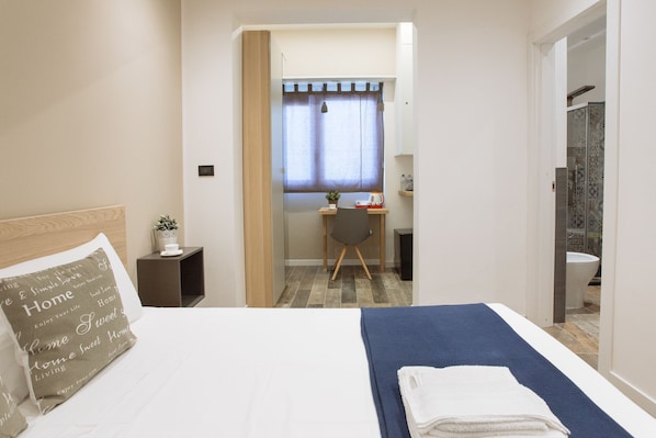 A bedroom with a bed, a desk, a chair, a small table with a plant, and a bathroom visible through an open door. - Politeama Luxury Suites (Palermo)