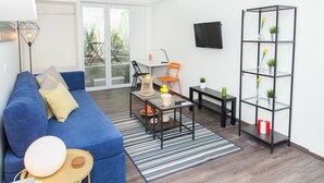 A modern living room with a blue sofa, a glass coffee table, a striped rug, and a black metal shelving unit with plants.