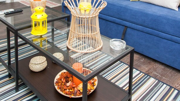 A modern living room with a blue sofa, a glass coffee table, and a striped rug.