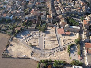 Vista aérea de un antiguo sitio arqueológico con ruinas rectangulares y edificios modernos circundantes.