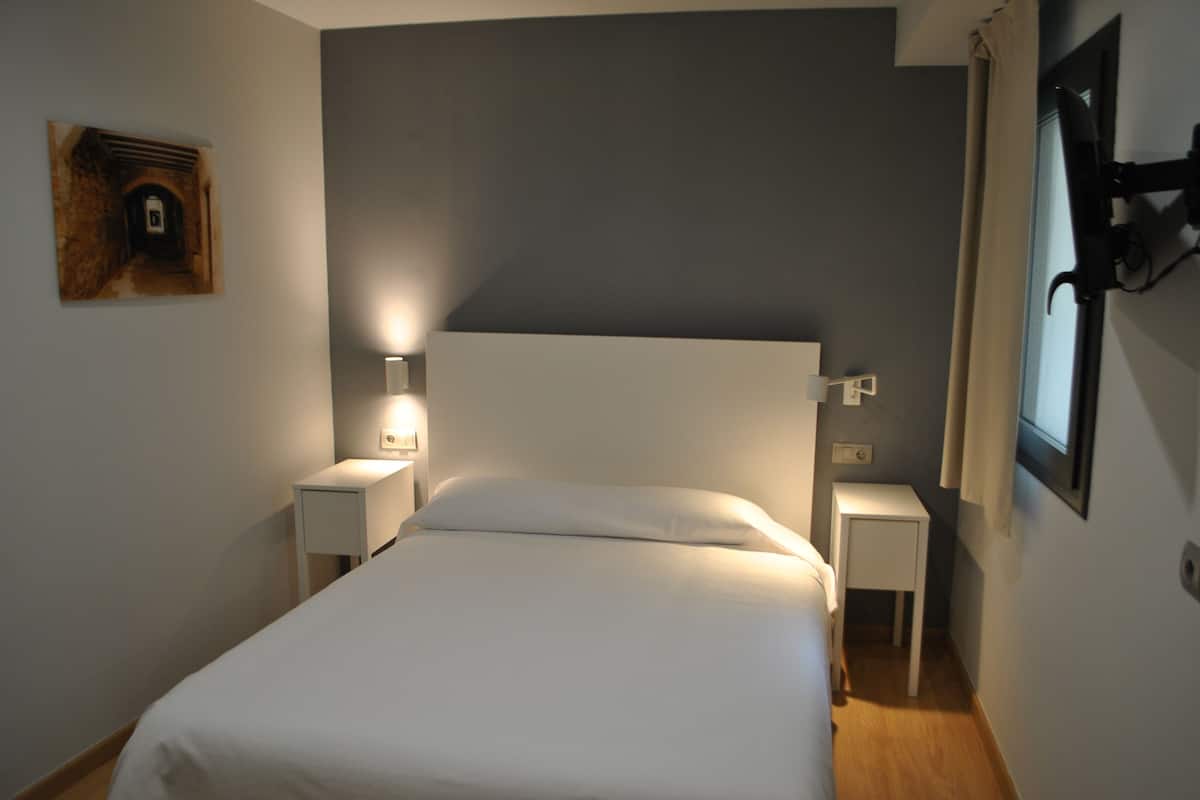 Um quarto com uma cama grande, duas mesas de cabeceira, um criado-mudo e uma luminária fixada na parede.