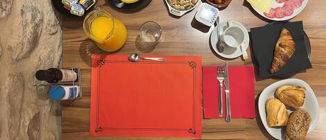Una mesa de desayuno con diversos alimentos, como frutas, nueces, queso y pasteles, junto con salsas y una bebida.