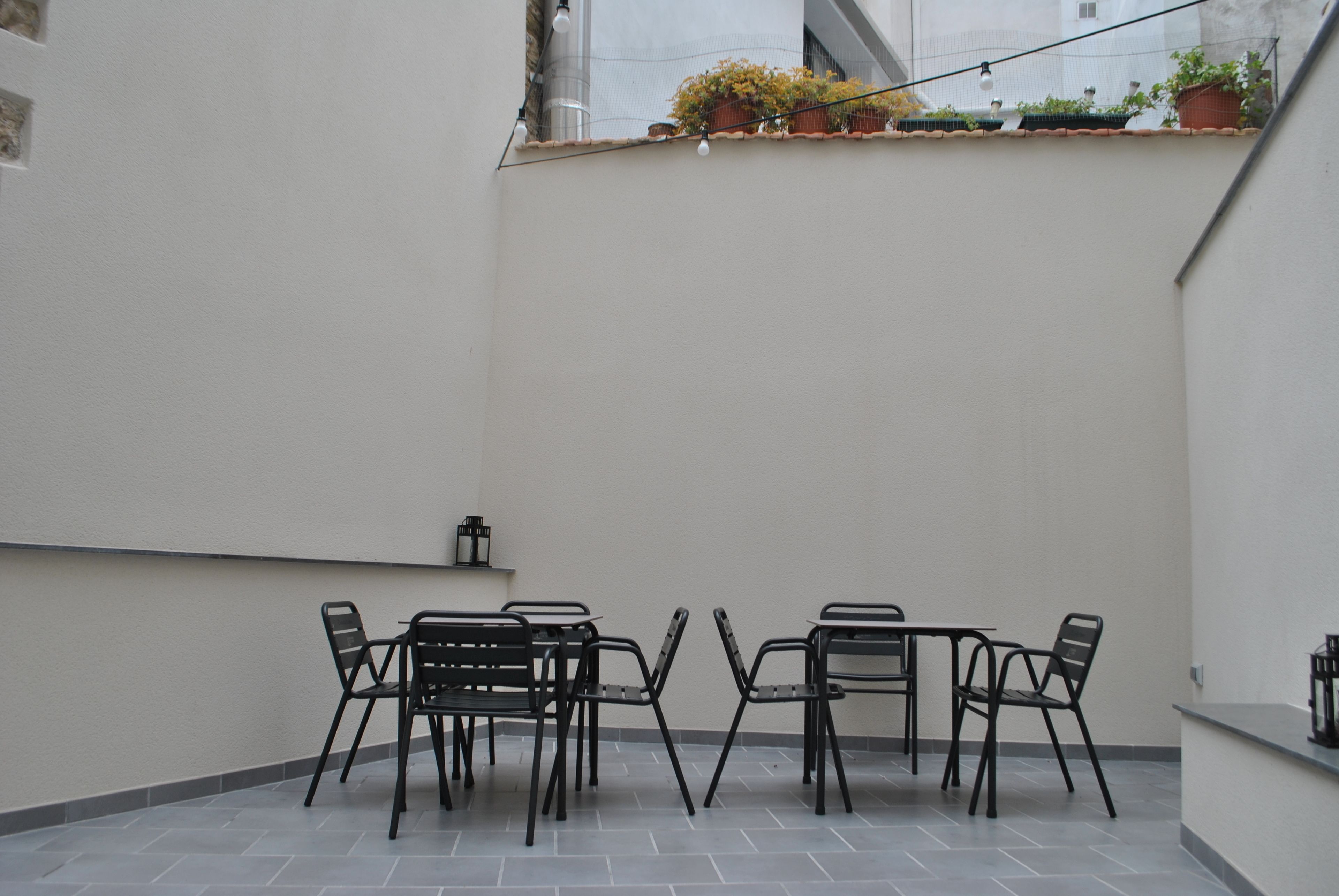 Une terrasse avec une table et des chaises, une petite étagère avec une lanterne et des plantes en pot accrochées au mur.
