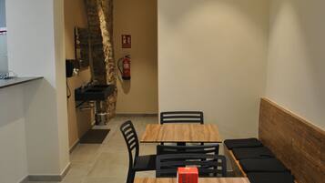 Un área de comedor con una mesa de madera y sillas negras, una pared de piedra y una pequeña zona de cocina con un lavabo y un extintor.