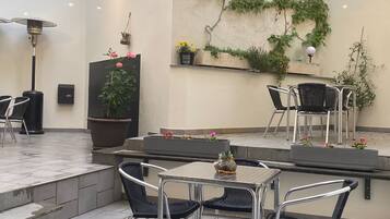 An outdoor patio area with metal chairs, a table, a potted plant, and a wall-mounted shelf with flowers.