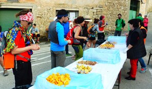 Un grupo de personas en un evento al aire libre, con una mesa que exhibe alimentos como naranjas y frutos secos.