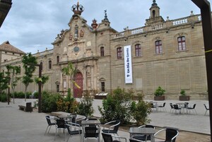 Un edificio histórico con una fachada destacada, un patio con asientos al aire libre y un cartel anunciando un evento especial.