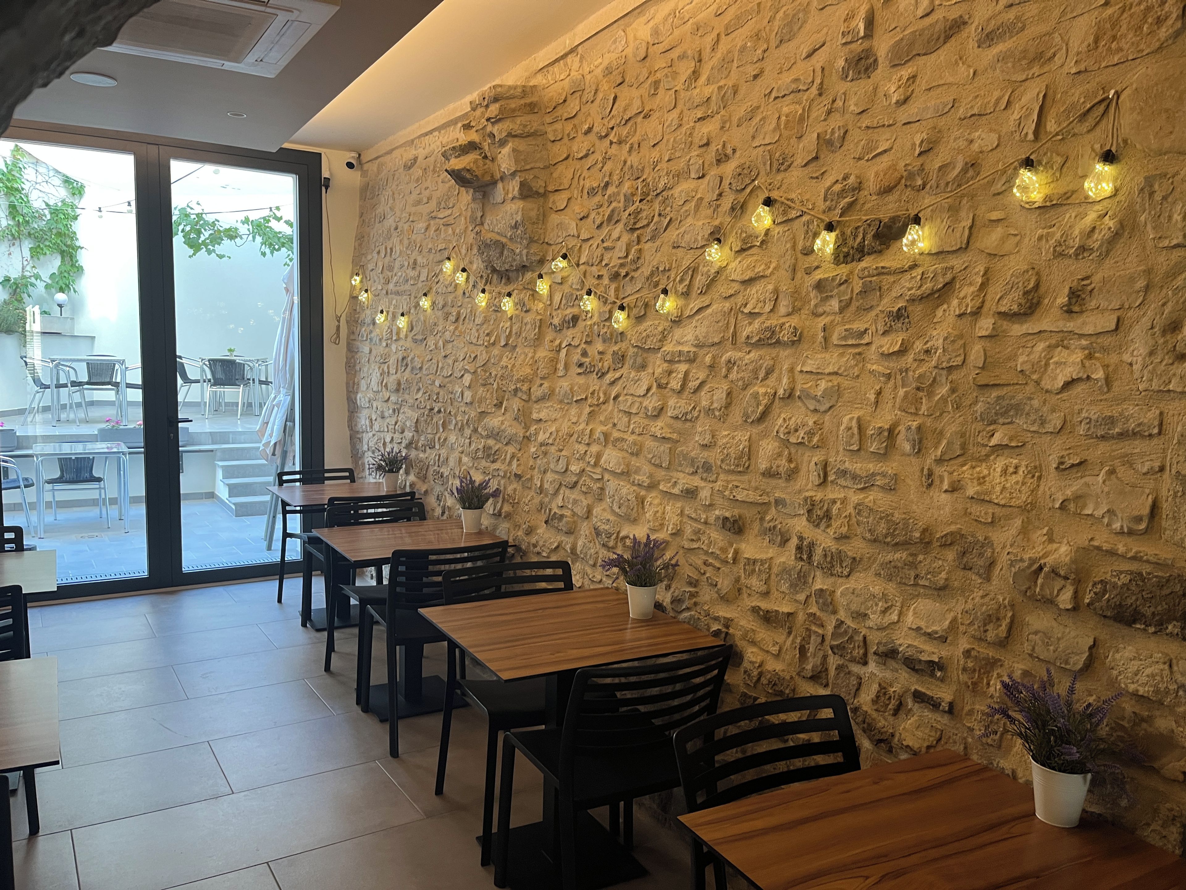 A restaurant interior with stone walls, wooden tables, and chairs, and string lights.