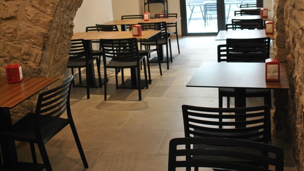 Un restaurant aux murs de pierre, aux tables en bois et aux chaises noires.