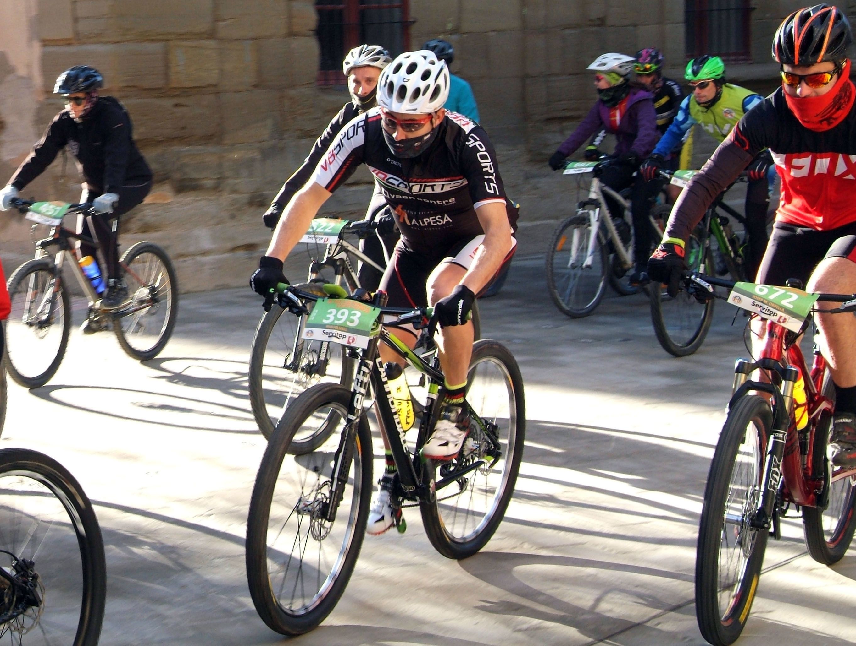 Un grupo de ciclistas en una carrera, usando maillots con números y cascos.