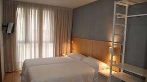 Une chambre d’hôtel avec deux lits, une tête de lit en bois, une échelle blanche et une grande fenêtre avec des rideaux.