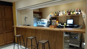 Un espace bar avec des tabourets, une machine à café et un assortiment de bouteilles d’alcool.