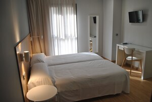 Habitación de hotel con dos camas, un escritorio, una silla, un televisor y una ventana con cortinas.