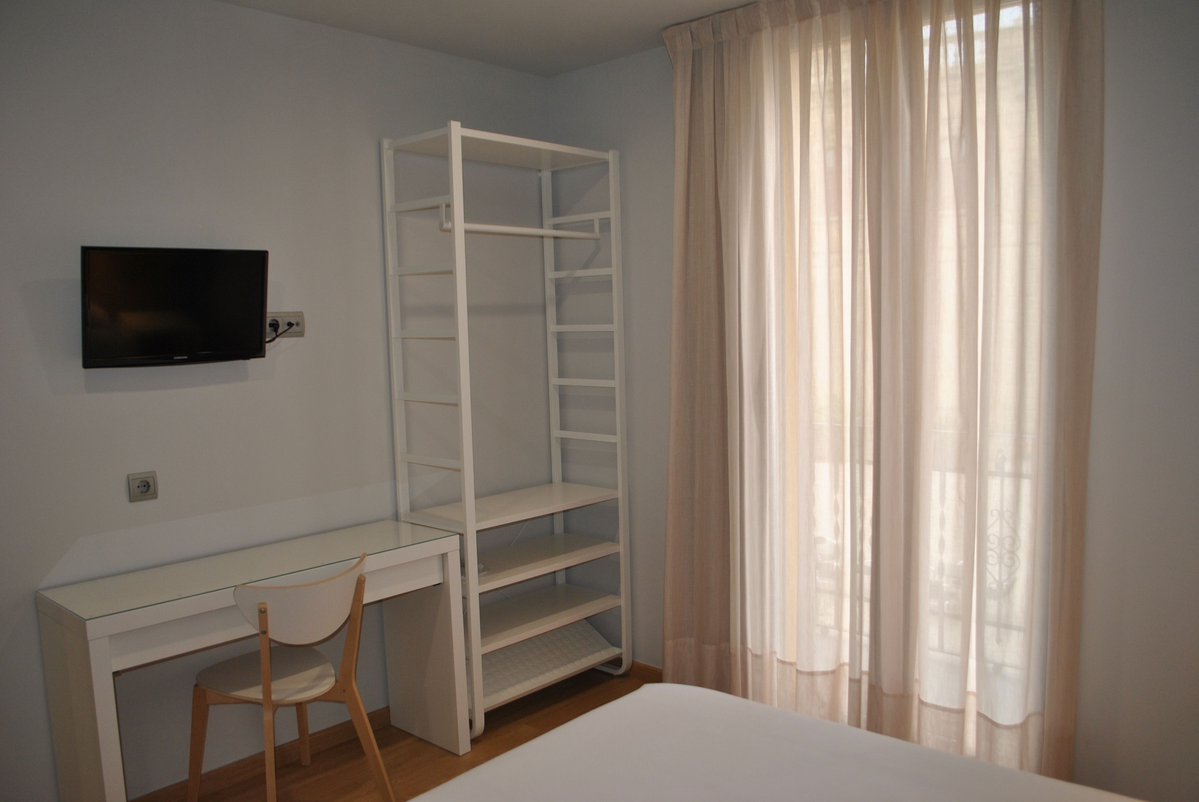 Un dormitorio con cama, escritorio, silla, televisor y armario.