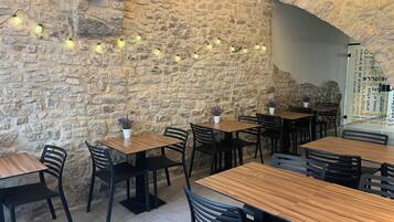 A restaurant interior with stone walls, wooden tables, black chairs, and string lights.