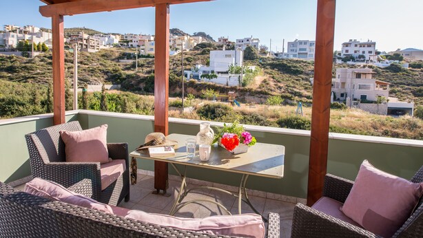 A covered outdoor seating area with wicker furniture and a table with flowers. - Ioanna's Home (Malevizi)