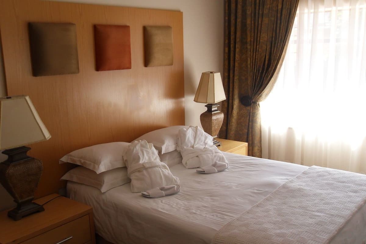A neatly made bed with white linens, a bedside lamp, and a nightstand with a lamp.