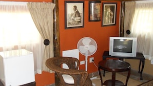 A room with a television, a fan, a chair, and a table.
