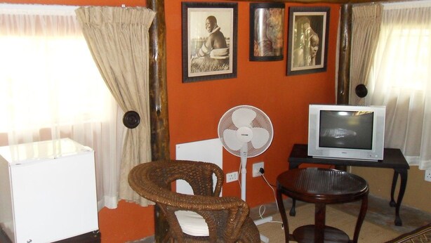 Una habitación con televisión, ventilador, una silla y una mesa.