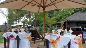 Un espacio de comedor al aire libre con mesas dispuestas para una recepción de boda, decorado con manteles blancos y cintas florales.