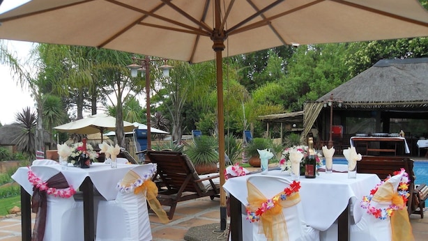 An outdoor dining area with tables set for a wedding reception, decorated with white tablecloths and floral sashes.