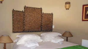 A hotel room with a bed, two bedside lamps, a green bedspread, and a decorative wall panel.