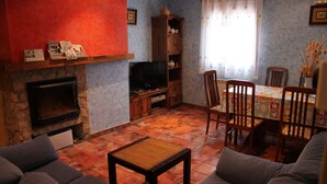 A living room with a fireplace, a television, and a dining area with chairs and a table. - El Rincon del Labrador (Castromonte)