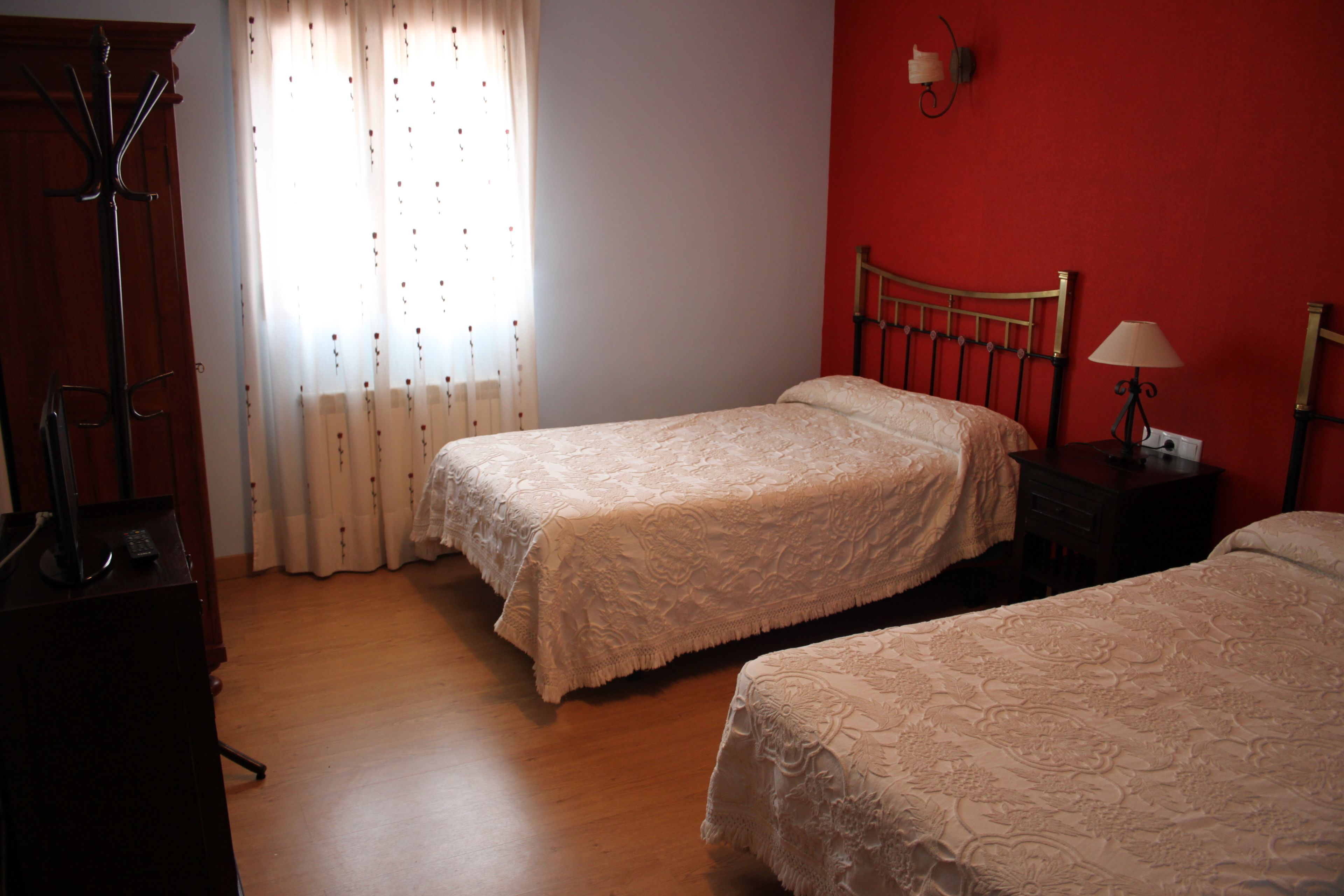 A room with two single beds, a wooden floor, a coat rack, and a window with curtains.