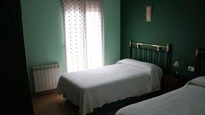A room with two single beds, a radiator, a window with curtains, and a wall-mounted lamp. - El Rincon del Labrador (Castromonte)